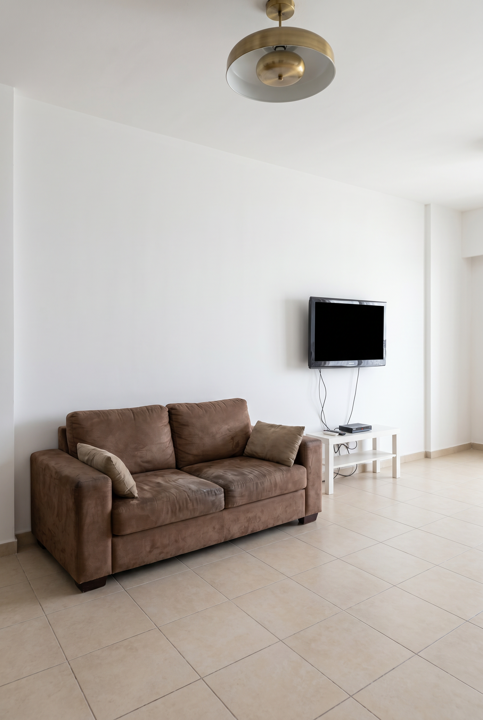 Berkeley Place entertainment room, pre-renovation. Dated 2010-era state, plain white walls, beige tile, basic LCD TV with visible cables.