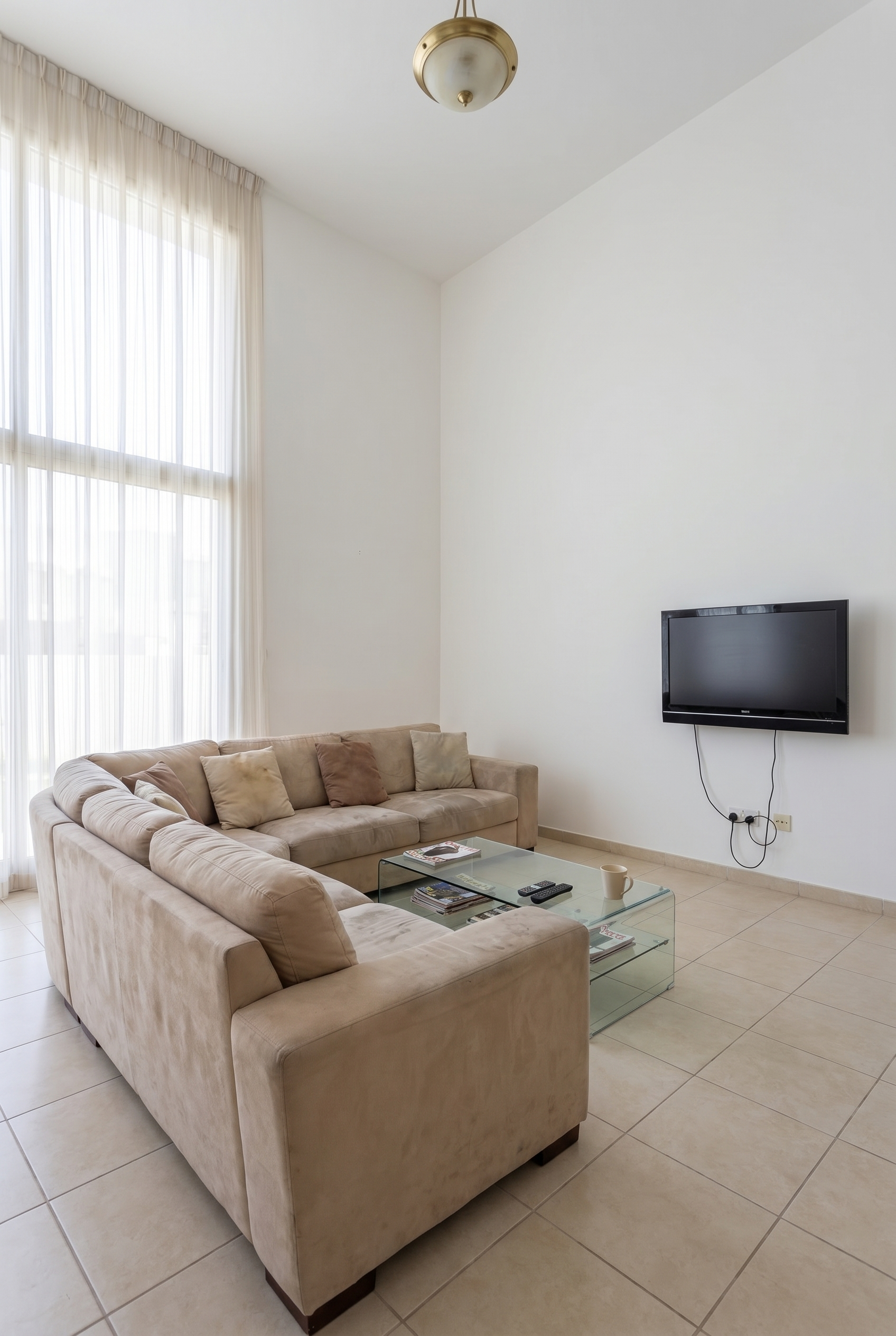 Dubai Hills apartment, pre-renovation. Dated 2010-era finishes, builder-grade walls, beige ceramic tile, worn beige sofa.